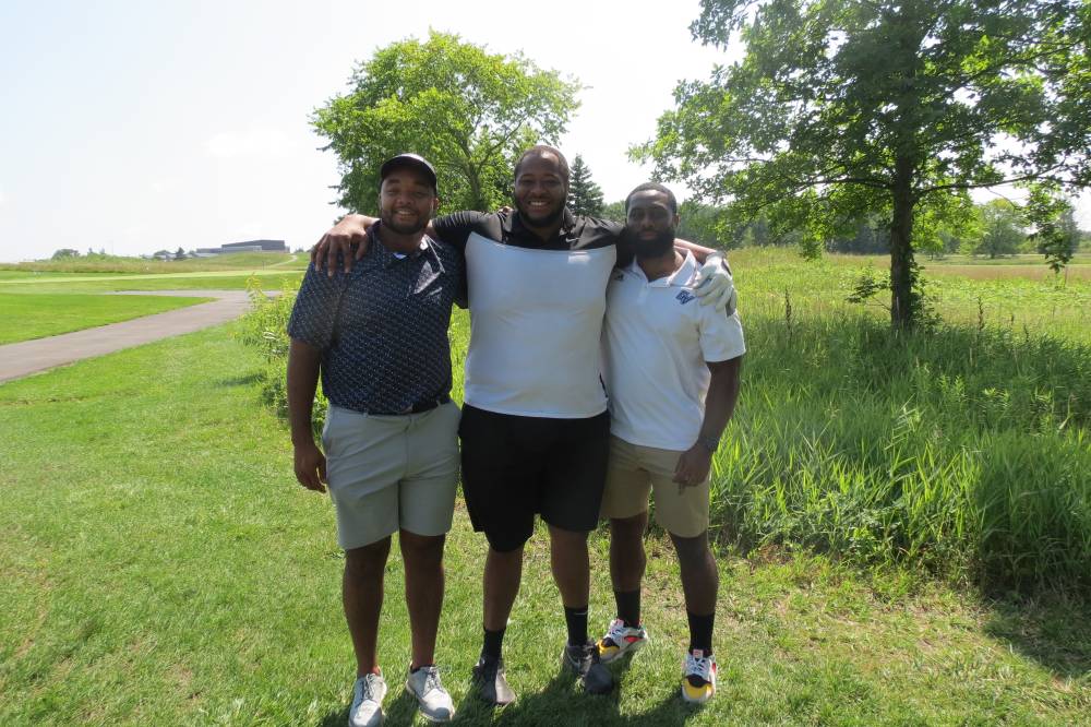 Three football alums standing on the golf course.